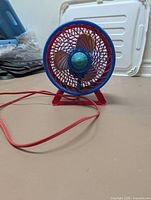 Front view of colorful plastic desk fan showing grill, blades and attached red cord