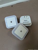 Three Uigos square plug-in LED night lights showing front and back, highlighting brand, sensor, and plug type.