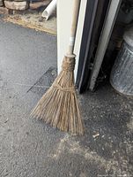 Full view of broom leaning against wall, showing straw head and wood handle