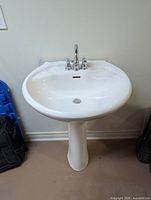 Front view of white pedestal sink on base with faucet attached