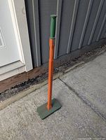 Full view of leaf tamper standing upright on pavement showing handle, shaft and base