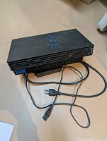 PlayStation 2 console showing top, front ports, accompanied by power cord