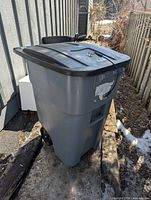 Front three-quarter view of grey Rubbermaid wheeled garbage can showing lid, handle and wheels