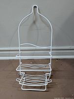 Front view of white metal shower caddy showing hook, shelves and soap dish
