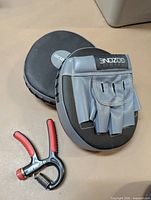 two black and grey Gozone focus mitts with red and black hand grip strengthener on tabletop