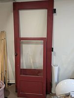 Full view of wood storm door showing upper and lower glass lite openings, red finish, hardware attached
