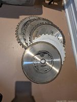 Stack of nine 10-inch circular saw blades showing brand markings, tooth wear