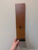 Front view of wooden magnetic board held by hand, showing two-tone finish and cube magnet
