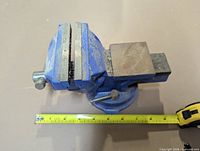 Top view of blue cast iron bench vise showing jaws, anvil pad and measuring tape for scale