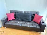 Full view of black faux leather futon with pillows