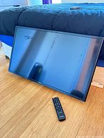 Front view of Samsung flatscreen TV resting on floor with remote control