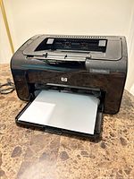 Front view showing HP LaserJet P1102w printer with paper tray open and sheet loaded