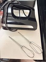 Black KitchenAid 5-speed hand mixer with two stainless-steel beaters on countertop
