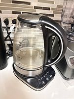 Front angled view of glass kettle on control base showing handle, spout, lid and control buttons