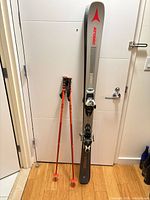 Atomic skis with bindings and ski poles leaning against wall
