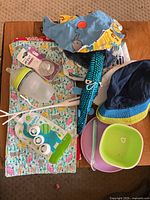 All items laid out on table showing variety of baby feeding accessories, hats, bibs, plush toy