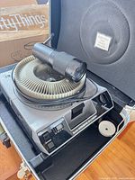 Projector inside hard case with carousel tray and lens attached, power cord visible