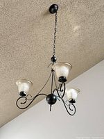 Oil-rubbed bronze three-light chandelier with frosted glass shades hanging from ceiling