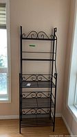 Full view of tall black wrought iron baker's rack with four shelves