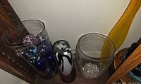 Group of glass pieces on shelf: two clear vases, yellow vase, black-white-pink vase, bowl
