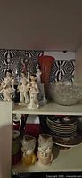 Figurines, orange vase, bubble glass bowl, plates and chick vases visible on shelving