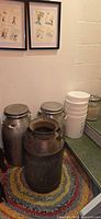 Three metal milk cans, two aluminum with lids, one steel without lid, plus stacked plastic buckets and glass jar