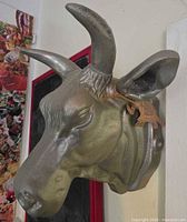 Left side view of silver cast metal cow head showing horns, ears, tag and mounting plate