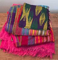 Stack of four colourful woven textiles showing colours and fringed edges