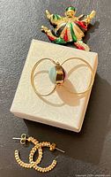All three jewelry pieces arranged: clown brooch, bypass ring on small box, hoop earrings below