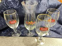 Front view of four Stella Artois goblets and one Hard Rock hurricane glass