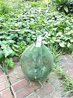 Full view of green aqua glass demijohn on brick path
