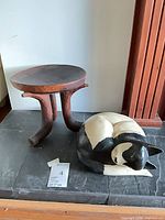Three-leg solid wood stool and painted wood sleeping cat sculpture on stone surface
