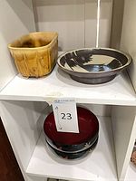 Top shelf showing yellow rectangular planter, brown/cream ceramic charger; lower shelf shows stacked lacquer bowls with red interiors