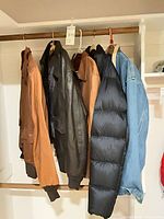 All five jackets hanging on closet rod: two brown leather bombers, one black leather bomber, black puffer coat, blue denim jacket