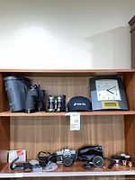 Shelf view showing camera, lenses, binoculars, and accessories together