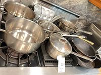 Overall lot showing stainless pots, pans, lids and muffin tin on stove