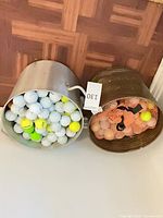 Two buckets side by side, one metal with loose balls, one brown with mesh bags of balls
