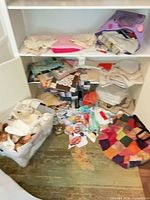 Shelving unit showing bins and piles of fabric scraps, quilt pieces and patchwork bag