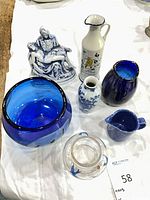 All seven items grouped together: blue glass bowl, blue glass vase, clear bird bowl, blue creamer, porcelain bud vase, Tuscany pitcher, Pietà figurine