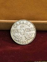 Reverse side of 1927 Canada 5 cent coin showing denomination and maple leaves