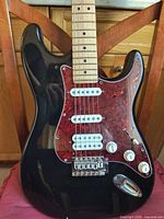 Front view showing black Strat body, tortoise pickguard, HSS pickups, controls and maple neck