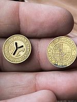 Both brass tokens obverse sides shown on fingertips