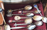 All nine silver plated souvenir spoons on burgundy cloth showing decorative handles and bowls