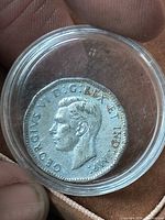 Obverse showing King George VI portrait inside clear capsule held by fingers
