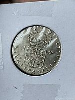 Reverse of coin in holder showing shield and motto