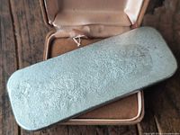 Pewter ingot bar resting on case showing top surface texture