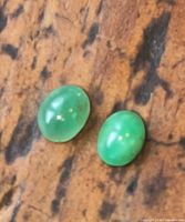Pair of green oval cabochon emeralds on wood surface