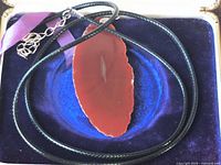 Full necklace showing agate slice pendant on black cord inside display box