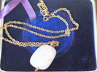Necklace laid in box showing gold-tone chain and rose quartz pendant