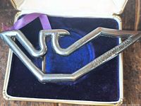 Front view of silver metal buckle showing stylised eagle form and Emporio Armani branding in presentation box